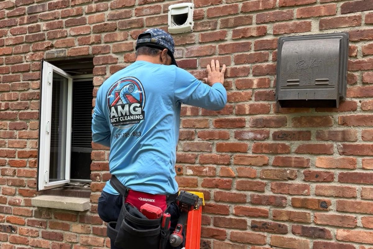 AMG technician working on an exterior dryer vent hood set into a red brick wall